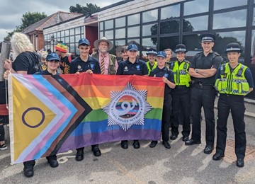 Jeff Cuthbert standing with officers and cadets in front of Pride flag 